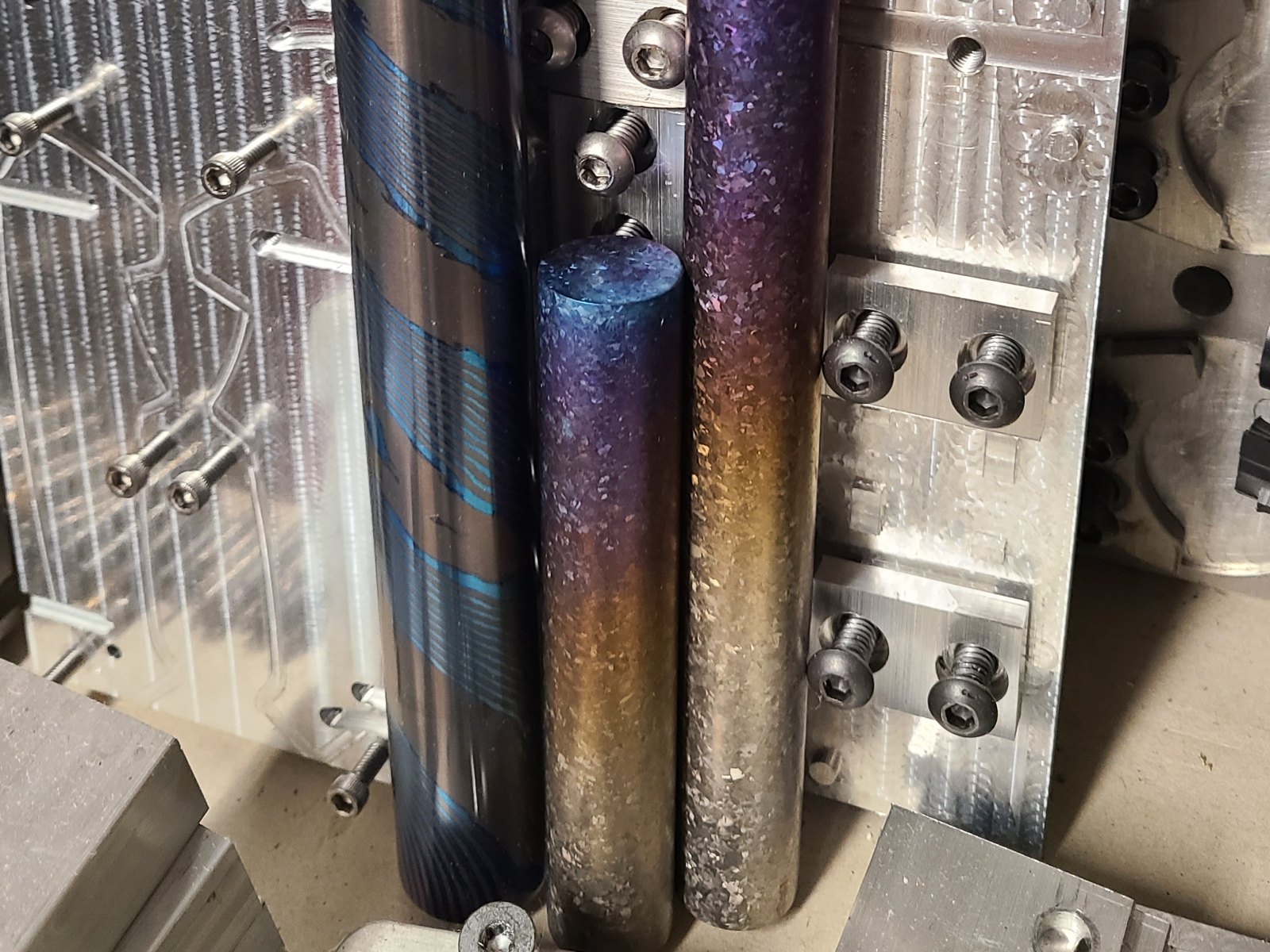 Three color-finished round bars standing in a machined fixture plate