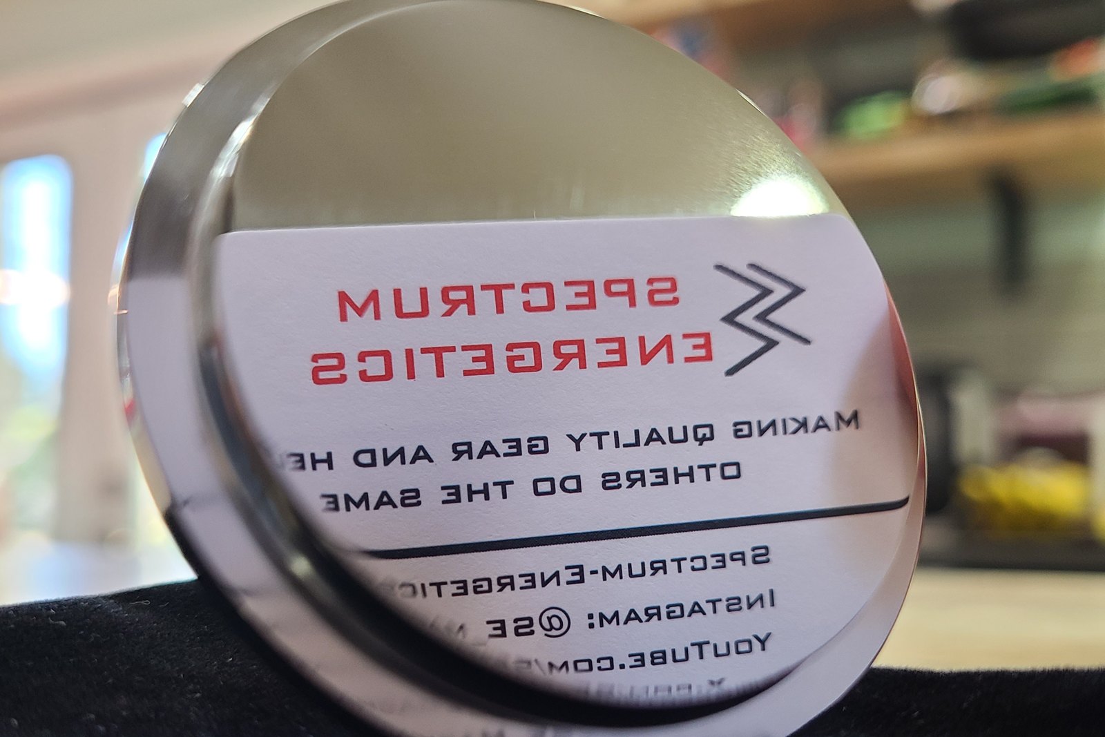 Mirror-polished metal disc reflecting a Spectrum Energetics business card