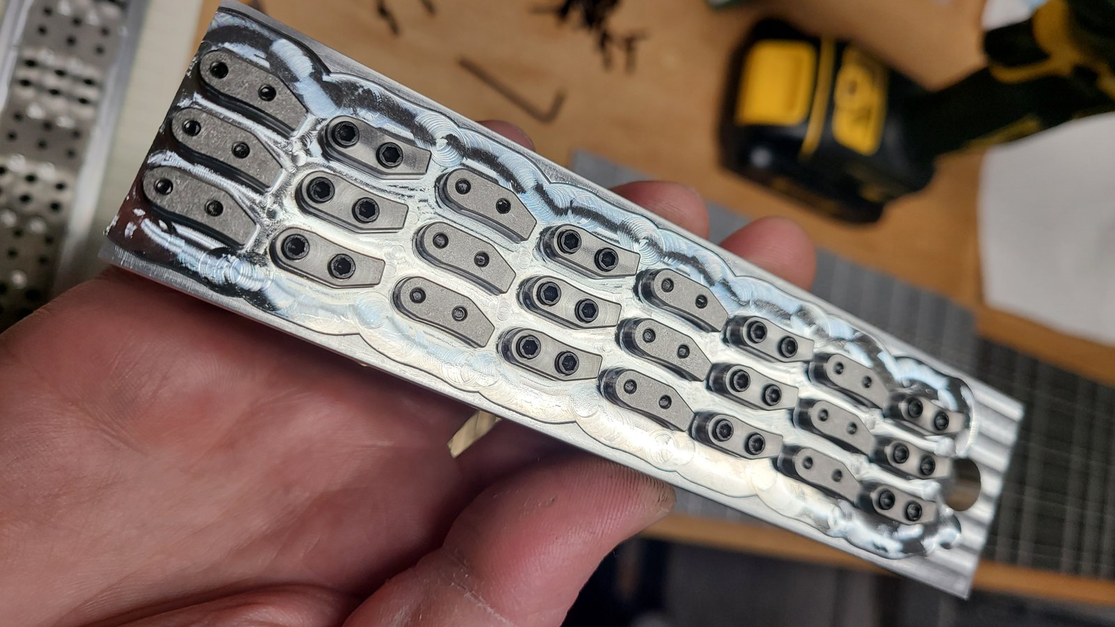 Hand holding a machined fixture plate with rows of small parts still in place
