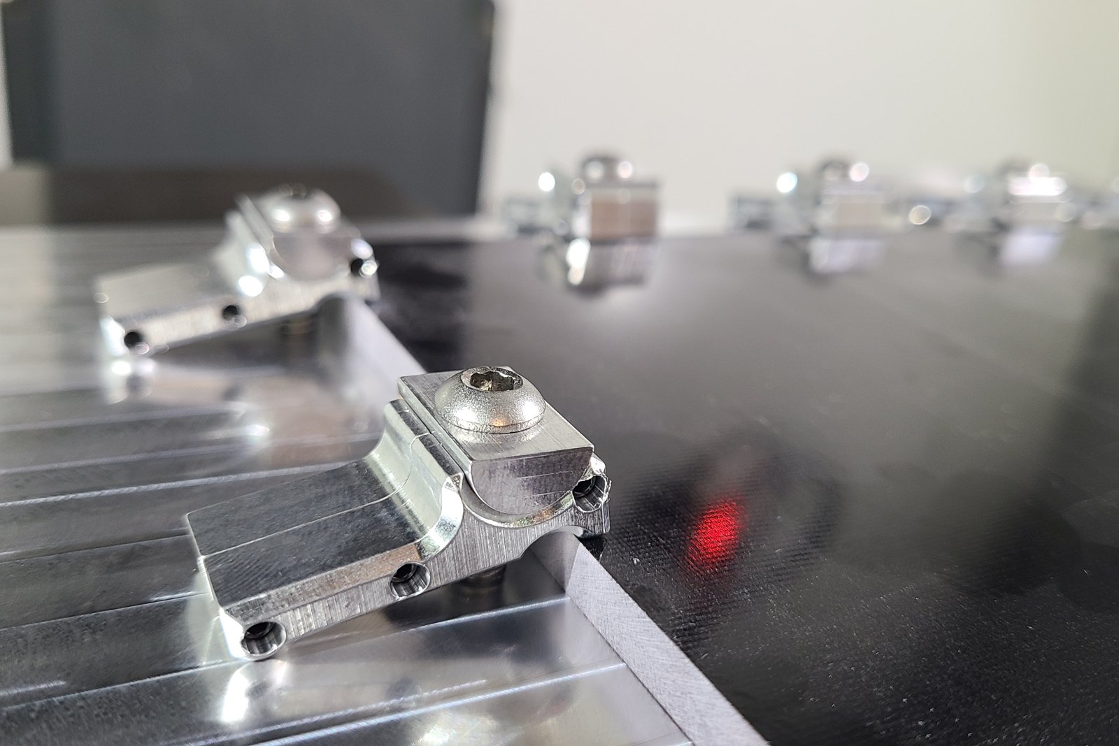 Machined clamps with button-head screws holding a black sheet on a fixture plate